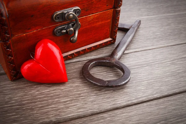 Trä bröstet med metalliskt nyckel och rött hjärta på bakgrund — Stockfoto