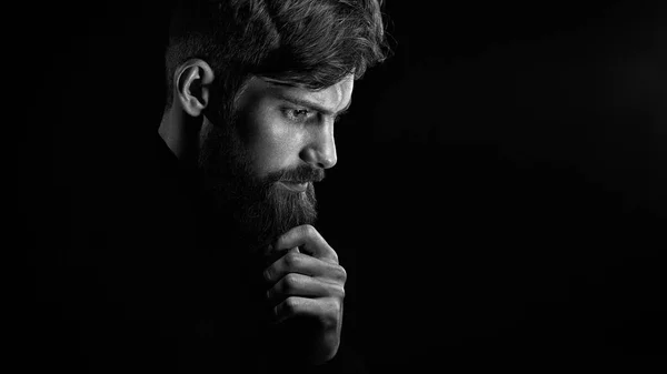 Puzzled young man touching beard looking down over black backgro — Stock Photo, Image