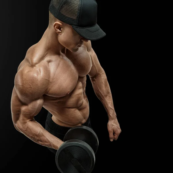 Gros plan d'un beau bodybuilder d'homme athlétique de puissance faisant des exercices avec haltère dans la main gauche. bodybuilder fort avec six pack, abdos parfaits, épaules, biceps, triceps et poitrine. Porter une casquette de baseball noire . — Photo