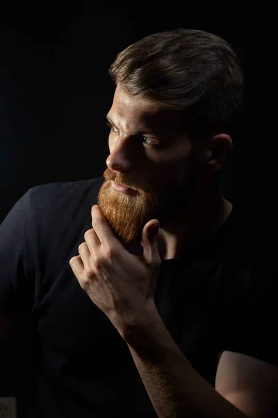 Atraente jovem pensativo olha para a distância acariciando sua barba — Fotografia de Stock