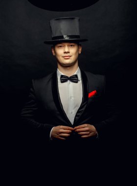 Siyah elbiseli bir boş silindir şapka ve siyah arka plan üzerine izole sihirli değnek tutan bir sihirbaz