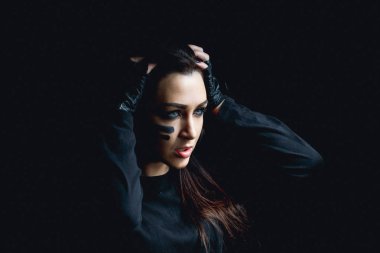 Koyu arka plan üzerinde güzel agresif kadın. Karanlık ve gizemli güzel bir kız gölge camoflauge boya ile yüzünde duruyor. 