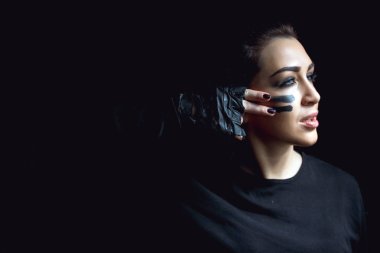 Koyu arka plan üzerinde güzel agresif kadın. Karanlık ve gizemli güzel bir kız gölge camoflauge boya ile yüzünde duruyor. 