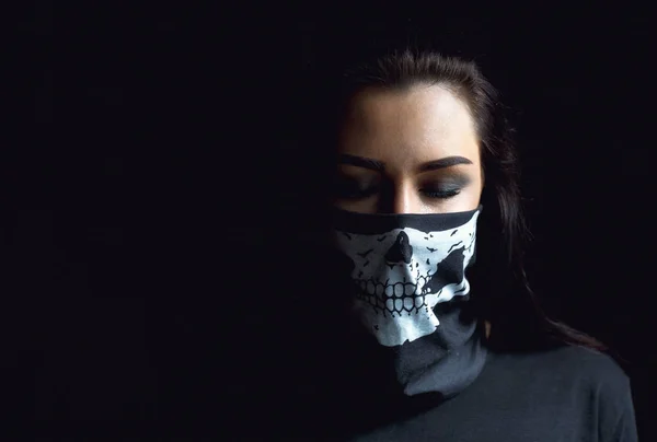 Beautiful aggressive woman over dark background. Sexy woman with black skull scarf over her face, studio closeup.