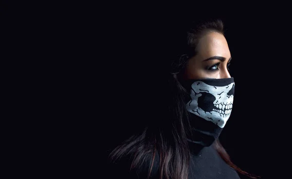 Beautiful aggressive woman over dark background. Sexy woman with black skull scarf over her face, studio closeup.