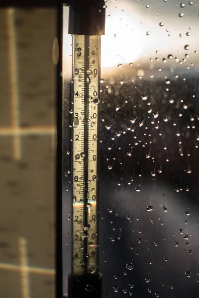 Daling van de temperatuur op een thermometer-schaal. Druppels regen op venster na een storm. Waterdruppels op het glas na regen. — Stockfoto