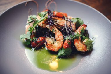 Pişmiş karides, karides ile baharat üzerinde arka plan taş. Kızarmış karides alakart bir tavada bir karanlık masa üstü üzerinde rosemary ile görüntüleyin. Karides restoranda kiraz domates ile dökme demir tava üzerinde. 