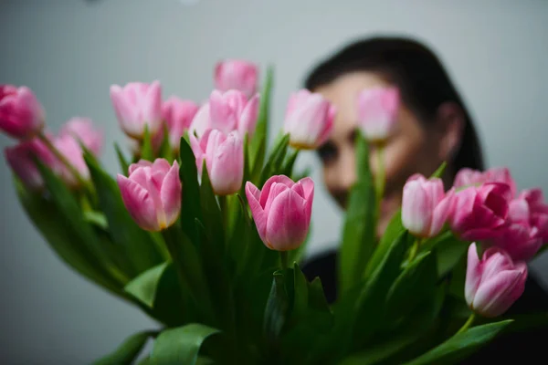 Young beautiful happy girl holding spring bouquet of tulips, posing on white background.  Portrait of attractive young woman with tulips is standing in light room and smiling. Happy international women\'s day! Celebrating 8th of March.