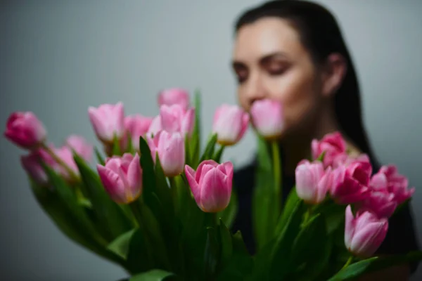 Young beautiful happy girl holding spring bouquet of tulips, posing on white background.  Portrait of attractive young woman with tulips is standing in light room and smiling. Happy international women\'s day! Celebrating 8th of March.