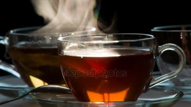 Bir fincan çay. Teabag şeffaf bir fincan sıcak su ile karanlık bir arka plan üzerine düşüyor. Su çay renginde boyanmıştır. 240 fps hızında çekim.