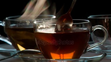 Çay küçük kaşıkla karıştırılır. Teabag şeffaf bir fincan sıcak su ile karanlık bir arka plan üzerine düşüyor. Su çay renginde boyanmıştır. 240 fps hızında çekim