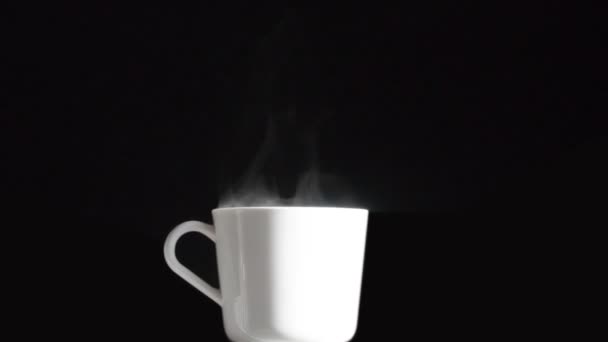 朝のホットドリンク カメラはゆっくりと明るい白いマグカップに近づいています そこから熱い蒸気が黒い背景にゆっくりと上昇します — ストック動画