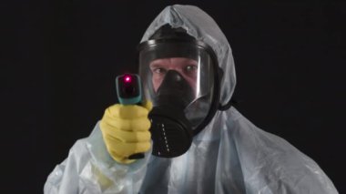 Koruyucu Maske olmadan yapamazsınız. Koruyucu giysili ve maskeli bir adam sıcaklığı uzaktan ölçüyor ve tıbbi destek veriyor.