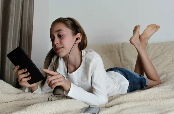 Девочка-подросток в наушниках играет на планшете — стоковое фото