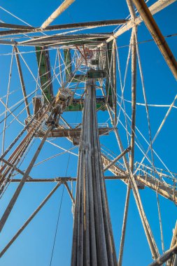 Drilling a well in winter at a northern oil and gas field. The drilling rig is covered in snow. Inside view from the bottom up. Polar frosty day. Blue sky.
