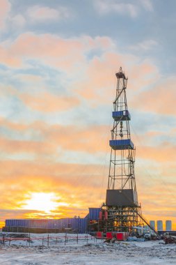 Oil and gas drilling rig in the northern tundra. Winter in the arctic. The sun of the polar day sparkles through the clouds. Backlighting. clipart