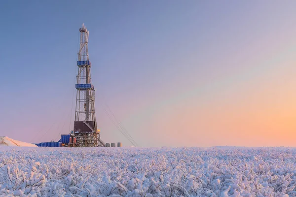 In a winter snow-covered tundra, a well is being drilled at an oil and gas field. Polar day. Beautiful sky. The drilling rig is covered in snow.