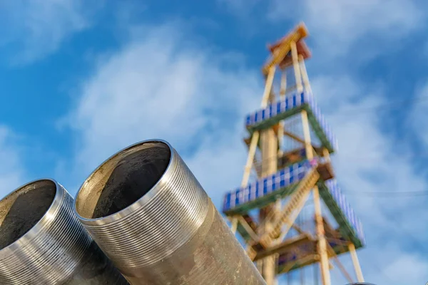 Petrol ve gaz kuyularını delmek için ön plandaki borularda. Arka planda, teçhizatın bulanık bir görüntüsü var. Bulutlu mavi gökyüzü.