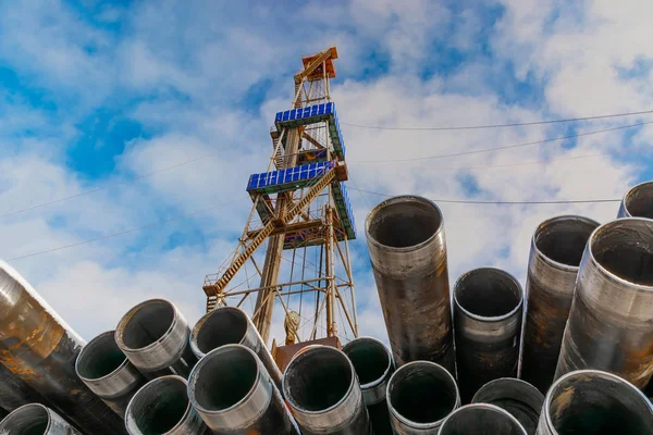 Petrol ve gaz kuyularını delmek için ön plandaki borularda. Arka planda bir sondaj kulesi var. Bulutlu mavi gökyüzü.