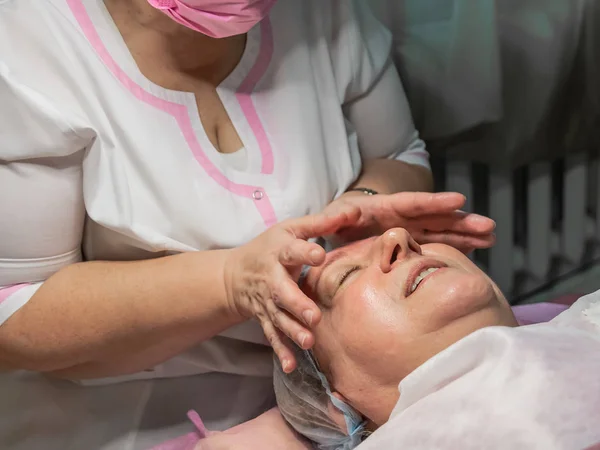 A cosmetic procedure with manual facial massage in a beauty salon is performed for an aged woman. Improving skin turgor, rejuvenation and healing.