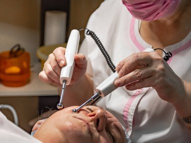 A cosmetic procedure with microcurrent injections in a beauty salon is performed for an aged woman. Improving skin turgor, rejuvenation and healing. clipart