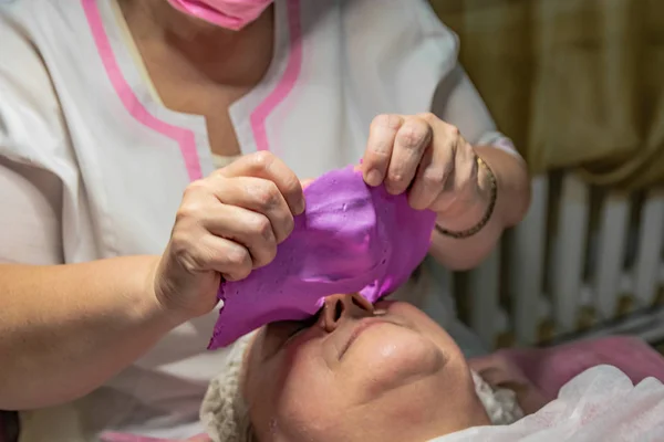 Cosmetic procedure with laying alginate masks on the face in a beauty salon. It is performed for an age woman. Improving skin turgor, rejuvenation and healing.