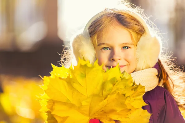 Menina feliz em earflaps com folhas de outono — Fotografia de Stock