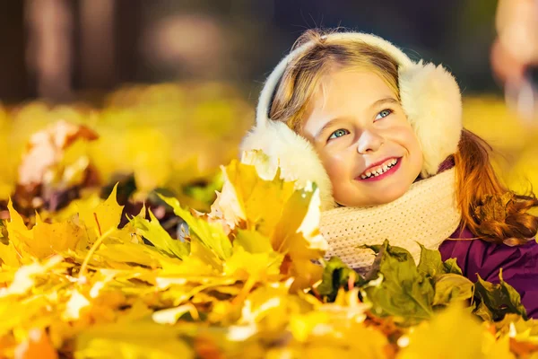 Menina em earflaps brincando com folhas de outono — Fotografia de Stock