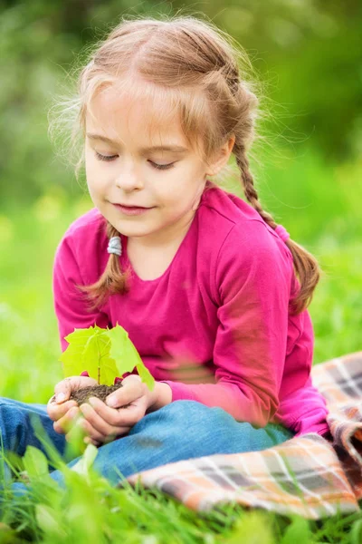 Menina segurando pequena planta verde em suas mãos — Fotografia de Stock