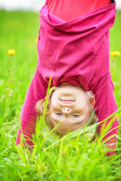 夏の公園の芝生の上に逆さまに立って幸せな少女 — ストック写真