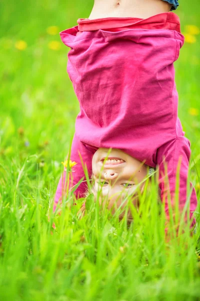 Happy little girl standing upside down on grass in summer park — Stock Photo, Image