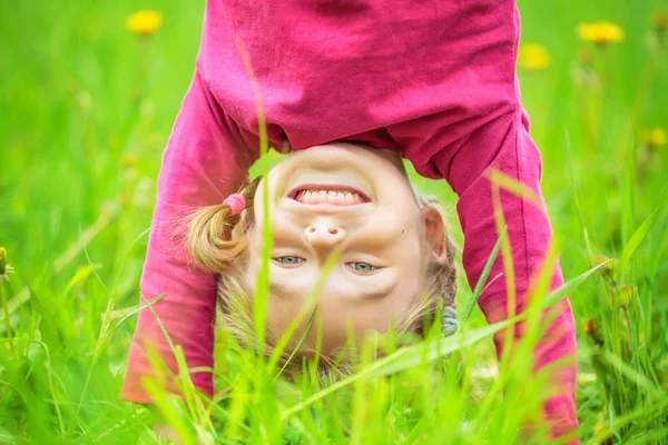 Happy little girl standing upside down on grass in summer park — Stock Photo, Image