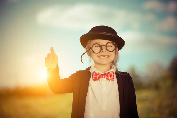 Lustiges kleines Mädchen in Fliege und Melone zeigt Daumen hoch. — Stockfoto