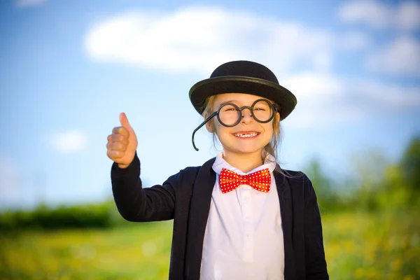 Lustiges kleines Mädchen in Fliege und Melone zeigt Daumen hoch. — Stockfoto