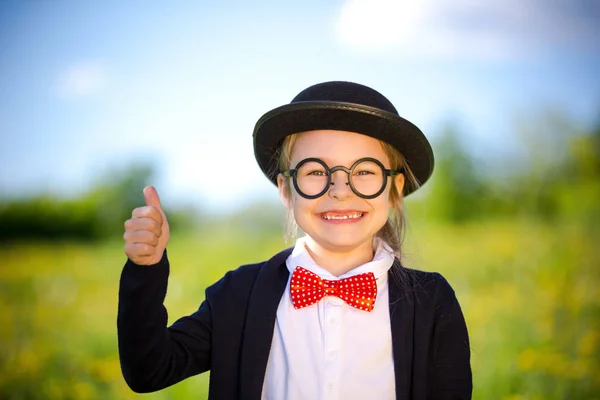 Lustiges kleines Mädchen in Fliege und Melone zeigt Daumen hoch. — Stockfoto