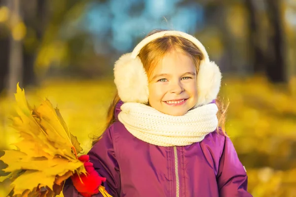 Happy little girl in earflaps with autumn leaves — Stock Photo, Image