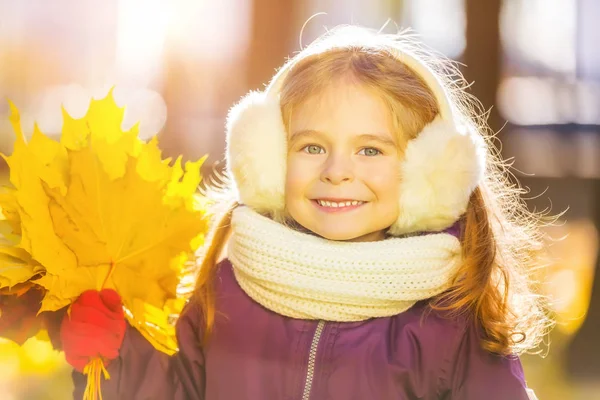 Menina feliz em earflaps com folhas de outono — Fotografia de Stock