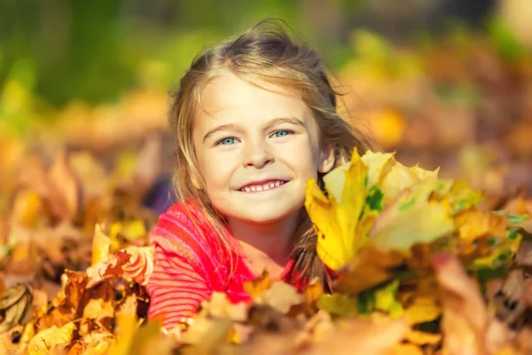 Happy little girl plays with autumn leaves — Stock Photo, Image