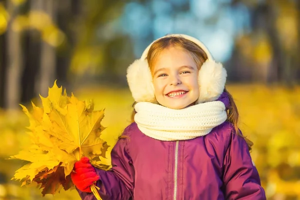 Bonne petite fille dans les oreillettes avec des feuilles d'automne — Photo