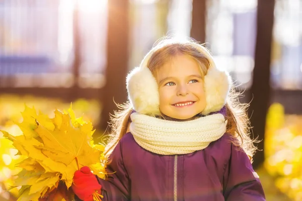 Menina feliz em earflaps com folhas de outono — Fotografia de Stock