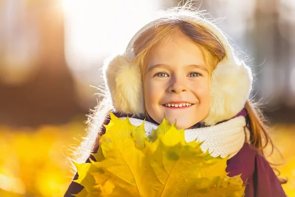 Menina feliz em earflaps com folhas de outono — Fotografia de Stock