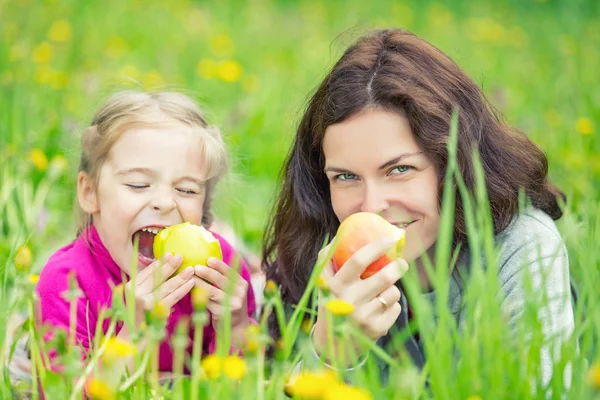 Mother and daughter eating apples on green summer meadow — Stock Photo, Image