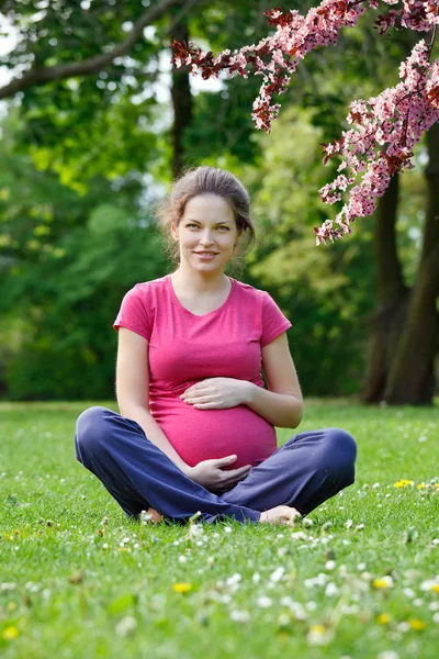 Mulher grávida relaxante no parque da primavera — Fotografia de Stock