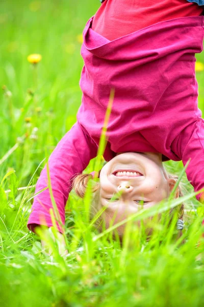 Happy little girl standing upside down on grass in summer park — Stock Photo, Image