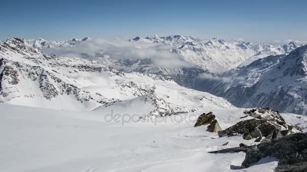 Sonniger Tag über Wolken in den schneebedeckten Winteralpen. Zeitraffer-Dolly über Felsen und Schneeverwehungen geschossen — Stockvideo