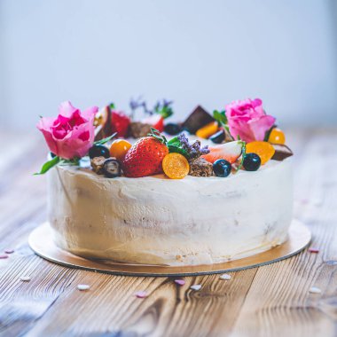 Taze meyveli tatlı beyaz cheesecake turtası ahşap masa arkasında haşhaş ve gül çiçekleri. Doğum günü, Sevgililer Günü ve kutlama için ideal bir hediye.