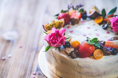 Taze meyveli tatlı beyaz cheesecake turtası ahşap masa arkasında haşhaş ve gül çiçekleri. Doğum günü, Sevgililer Günü ve kutlama için ideal bir hediye.