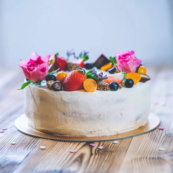 Taze meyveli tatlı beyaz cheesecake turtası ahşap masa arkasında haşhaş ve gül çiçekleri. Doğum günü, Sevgililer Günü ve kutlama için ideal bir hediye.