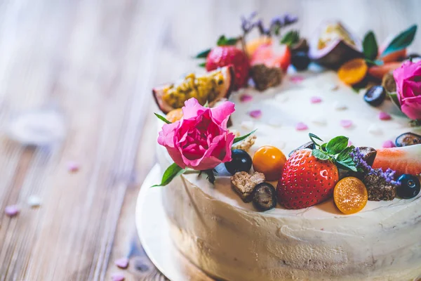 Taze meyveli tatlı beyaz cheesecake turtası ahşap masa arkasında haşhaş ve gül çiçekleri. Doğum günü, Sevgililer Günü ve kutlama için ideal bir hediye.