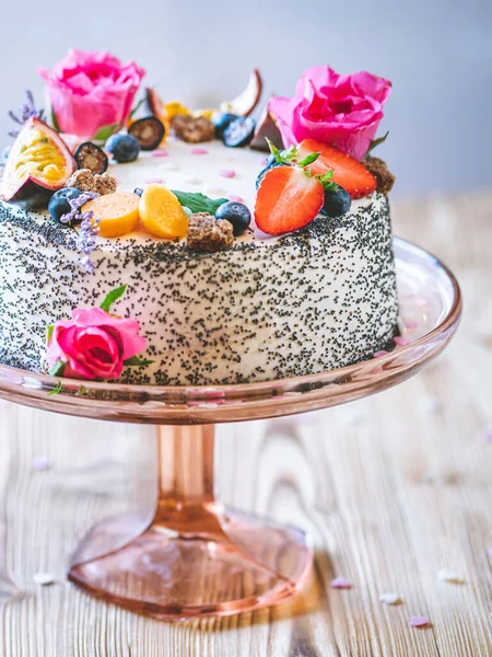 Taze meyveli tatlı beyaz cheesecake turtası ahşap masa arkasında haşhaş ve gül çiçekleri. Doğum günü, Sevgililer Günü ve kutlama için ideal bir hediye.